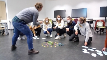 Studenten ordnen beschriftete Kärtchen auf dem Fußboden eines Seminarraums.